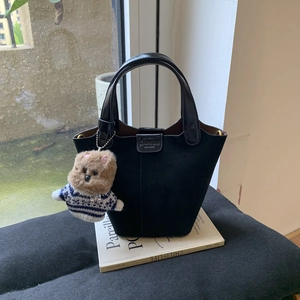 Detail of black leather bucket bag with a cute brown teddy bear plush charm