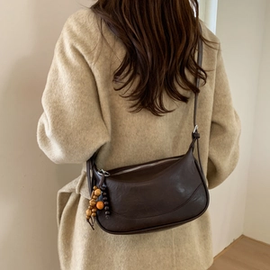 Detail of dark brown crescent bag with bohemian bead tassels on oatmeal winter coat