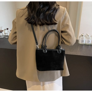 Detail of black suede bucket bag featuring a unique knotted handle and embossed logo design