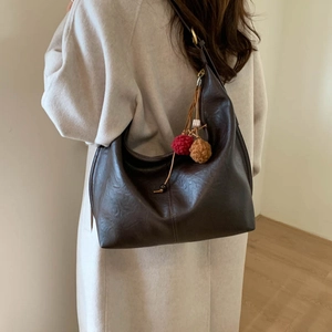 Detail view of a large brown leather shoulder bag with a decorative plush charm