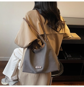 Detail of dark canvas hobo bag with leather straps on model in beige coat