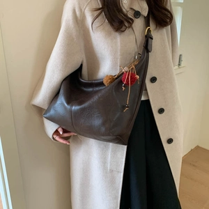 Model wearing a deep brown leather shoulder bag with decorative pompom and bead charm