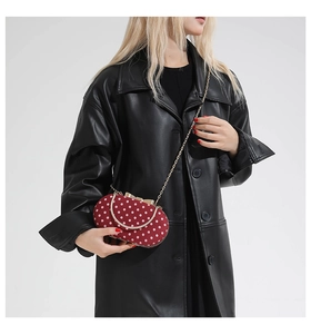 Polka dot red handbag with gold chain strap shown on a black leather coat model