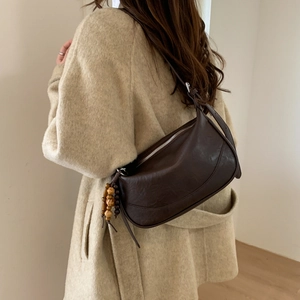 Detail of dark brown leather shoulder bag with vintage texture and wooden bead charm