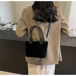 Detail of black suede bucket bag with camellia embossing shown in a café setting