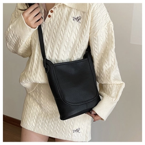 Detail view of black lychee grain leather bucket bag worn with a white knit outfit