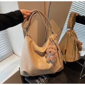 Detail of a beige PU leather bucket bag with a plush puppy charm and brand label