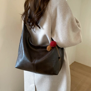 Macro shot of dark brown faux leather tote bag with stylish plush ball charms in use