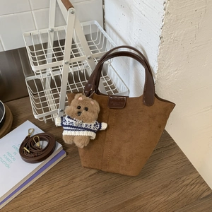 Detail of brown suede tote bag with leather handle, strap, and plush bear charm