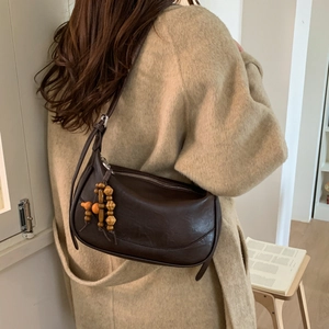 Detail of dark brown leather crescent bag with wooden bead pendant on model's shoulder