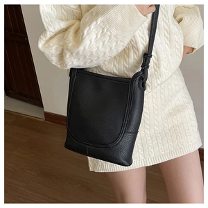 Chic black litchi grain leather bucket bag styled as a crossbody over a white sweater