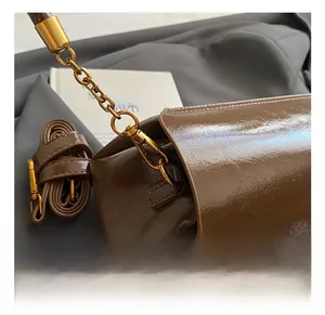 Gros plan sur les crochets dorés et la bandoulière en cuir marron brillant d'un sac à main