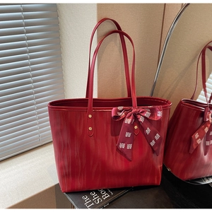 Detail of red tote bag with wavy faux leather texture and a festive red satin bow charm