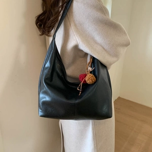 Detail of matte black leather hobo bag with dual-tone plush ball charm on a model