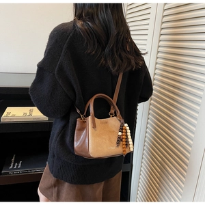 Detail der Vintage-Eimertasche mit Holzperlenquaste und Ledertextur an einem Modell