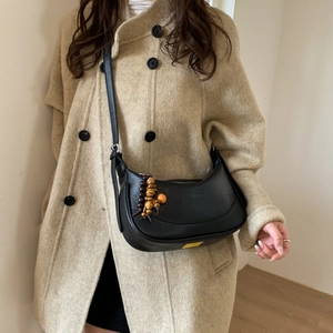 Detail of black leather hobo bag with vintage wooden beads on beige coat