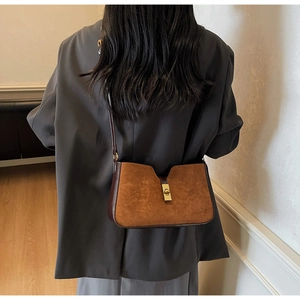 Détail du sac seau en daim marron avec fermoir doré et design en V porté par le modèle