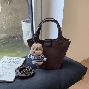 Detail of dark brown suede bucket bag with leather strap and cute puppy pendant accessory