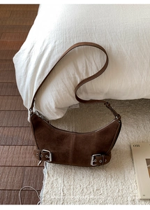Close-up of brown suede crescent bag with silver buckles in a cozy home setting