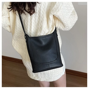 Detail of black pebbled leather crossbody bag with U-stitch and long strap on model