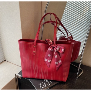 Detailed view of red tote bag with wave texture and festive silk scarf tied on handle