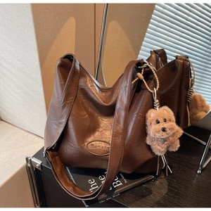 Macro detail of dark brown pleated tote bag with brand logo and plush dog charm