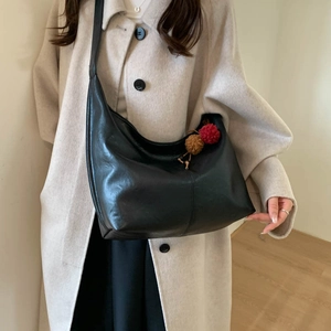 Detail of black large hobo shoulder bag with a cute red and brown pompom charm