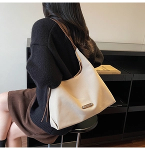 Detail of cream canvas tote bag with brown leather strap worn by model in minimalist setting