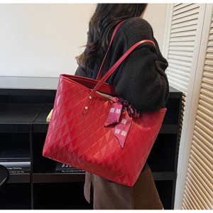 Detail of red quilted tote bag featuring a double shoulder strap and a decorative silk scarf