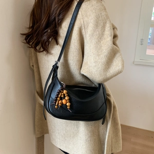 Detail of a black crescent hobo bag with unique wooden bead tassel decoration on a model