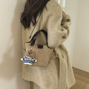 Detail of khaki suede bucket bag with leather handles and cute plush dog pendant charm