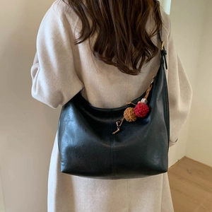 Detail of black crescent shoulder bag featuring soft textured leather and plush pom-poms