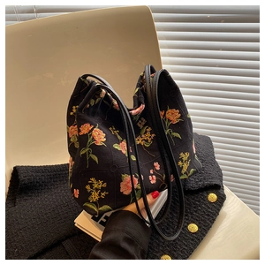 Detail of floral embroidery on a black canvas bucket bag styled with a tweed jacket