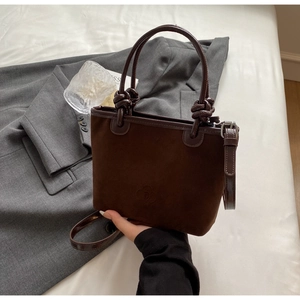 Detail shot of a dark brown suede bucket bag with a round handle and knotted accents