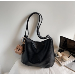 Detail of black pleated leather tote bag with a small plush bear charm on office desk