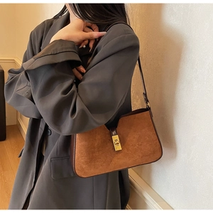 Gros plan d'un sac bandoulière en daim marron avec fermoir doré sur une veste grise