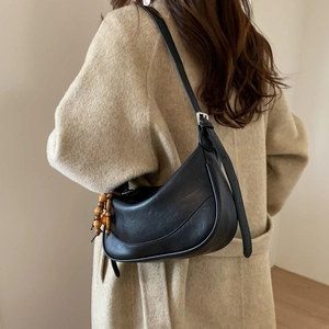 Detail of vintage black crescent shoulder bag with wooden bead charm on a beige wool coat