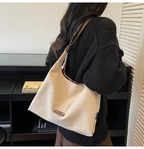 Detail of cream tote bag with brown leather straps shown on shoulder with black sweater