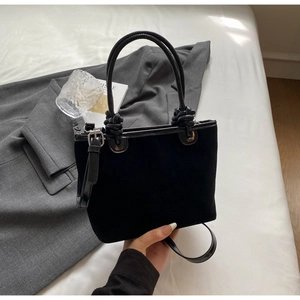 Detail of black suede bucket bag with leather handles and adjustable shoulder strap