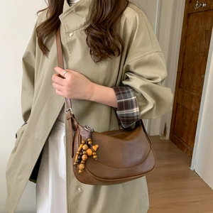 Brown vintage half-moon shoulder bag with wooden bead pendant on a beige trench coat
