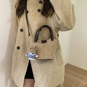 Detail of khaki suede bucket bag featuring brown leather straps and cute bear charm