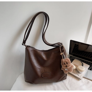 Detail of dark brown leather bucket bag featuring a Banatu logo and plush bear charm