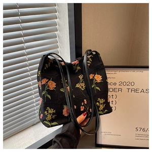 Detail of colorful floral embroidery and leather strap on a black canvas bucket bag