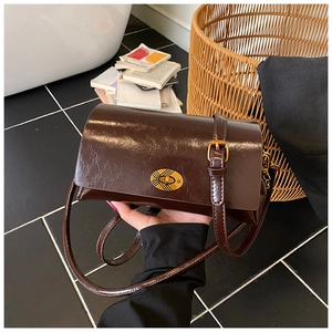 Détail du sac bandoulière en cuir brillant marron foncé avec boucle ovale dorée vintage