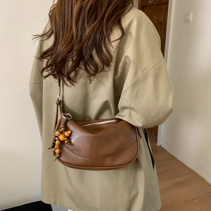 Brown vintage dumpling bag with wooden bead charm worn with a beige trench coat