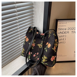 Detail of colorful floral embroidery on a black canvas bucket bag with slim shoulder straps