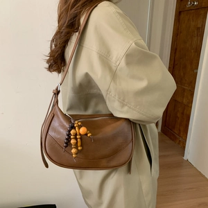 Close-up of retro brown half-moon bag with wooden bead pendant and smooth PU leather
