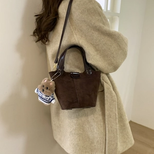 Dark brown suede bucket bag with leather handles and a cute puppy plush charm on model