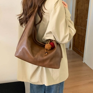 Detail of a large brown shoulder bag with plush ball charms on a casual outfit