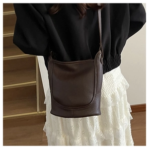 Detail view of large brown pebble leather crossbody bucket bag on a model in black coat